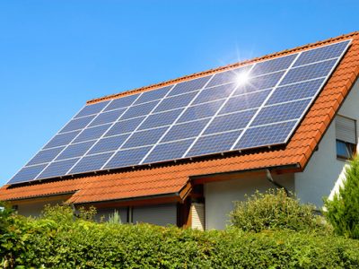 Solar panel on a red roof reflecting the sun and the cloudless blue sky